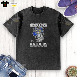 Top I May Live in Nebraska But I'm a Raiders Fan Forever washed t-shirt displayed on a hanger in casual setting.
